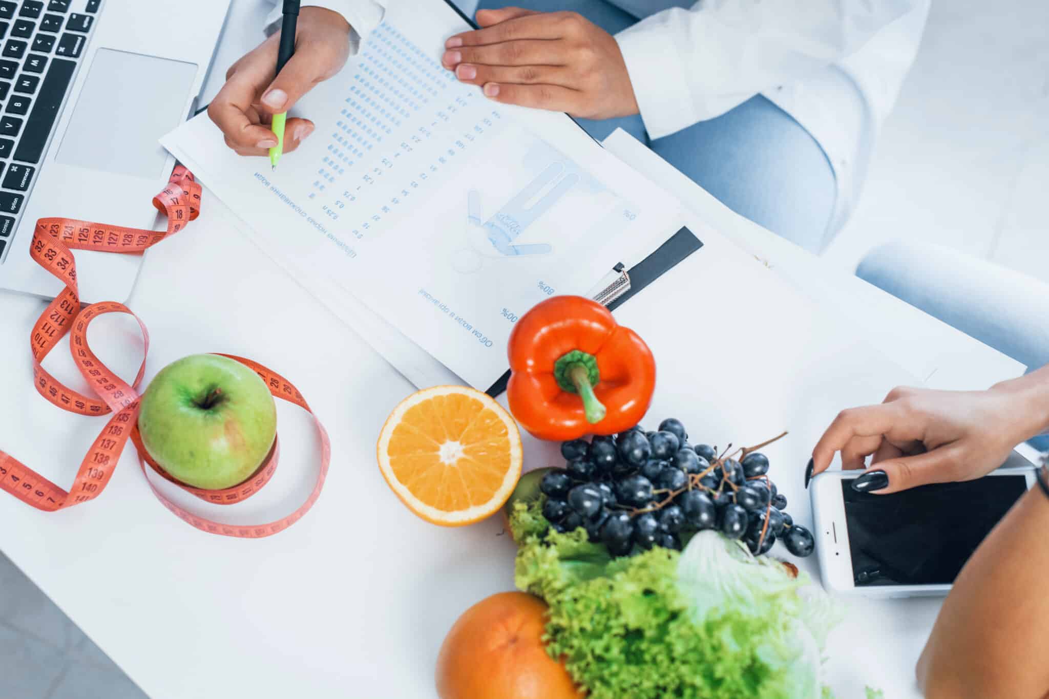 Schreibtisch mit Obst, Gemüse und Unterlagen - Draufsicht einer Ernährungsberaterin, die Beratung anbietet